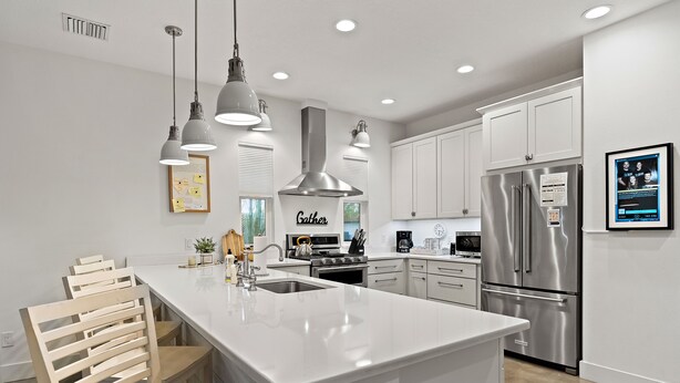 A modern kitchen with white cabinetry, stainless steel appliances, pendant lighting, and a central island.