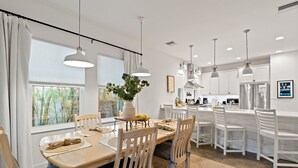 A modern kitchen with white cabinetry, pendant lighting, and a dining area with wooden chairs and a table set for four.