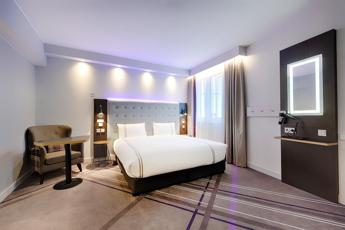 Ein Hotelzimmer mit Bett, Stuhl, Schreibtisch und Schminktisch mit Spiegel.