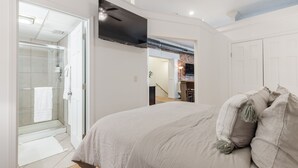A bedroom with a bed, a TV mounted on the wall, and a glass shower enclosure.