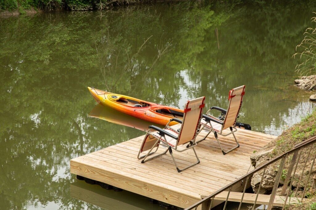 A wooden dock with two beach chairs and a yellow kayak on the water.