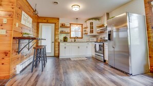 Une cuisine avec des murs en bois, des armoires blanches, un réfrigérateur en acier inoxydable et un tabouret de bar.