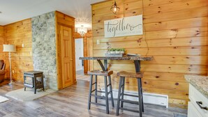 L’intérieur chaleureux d’un chalet avec un mur en pierre, un lambris en bois, un coin bar avec des tabourets et un lustre.