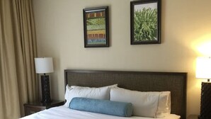A hotel room with a large bed, a ceiling fan, two framed pictures on the wall, and a nightstand with a lamp. - Amazing 3 bedroom condo (Philipsburg)