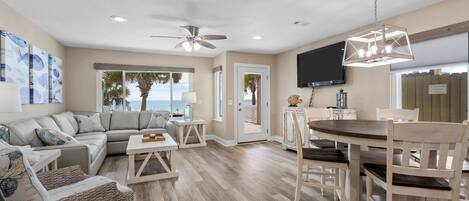 A spacious living area with a large sofa, a dining table, and a ceiling fan.