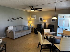 A living room with a gray sofa, two black chairs, a glass dining table, and a ceiling fan. - Your place in Paradise Island. (Marco Island)