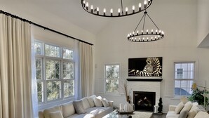 A spacious living room with a large window, a fireplace, and a modern chandelier. - SARATOGA DREAM!-Lake community close to Track and Downtown (Saratoga Springs)
