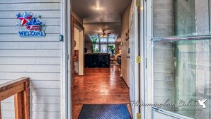 Une façade en bois avec une pancarte « Bienvenue », une porte vitrée et un couloir menant à un espace de vie.