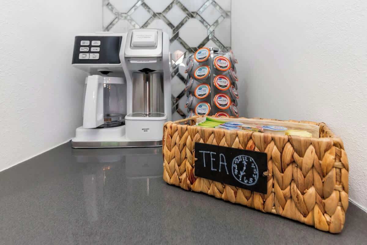 A coffee machine, a basket of tea bags, and a woven basket labeled 'TEA' on a countertop.