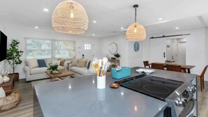 Una cocina moderna con una isla central, lámparas colgantes de mimbre y una zona de comedor con mobiliario de madera.