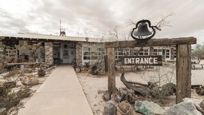 A rustic building with a stone facade, a wooden entrance sign, and a bell above the door.
