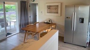 A modern kitchen with a wooden table, chairs, a refrigerator, and a clock on the wall.