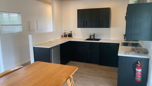 A compact kitchen with dark cabinets, a wooden table, and a fire extinguisher.