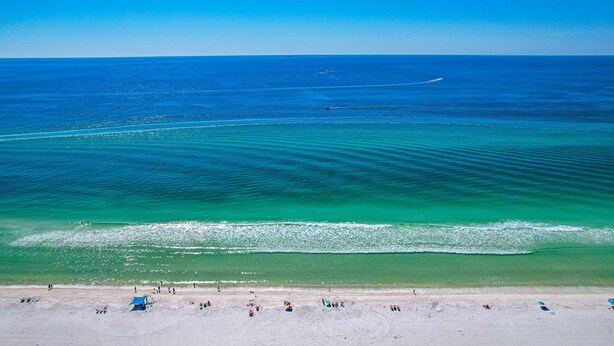 Ein Strand mit klarem türkisblauem Wasser, einem sandigen Ufer und einigen Sonnenschirmen.