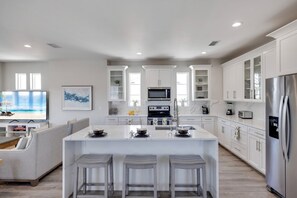 A modern kitchen with white cabinetry, a central island with stools, a built-in microwave, and a stainless steel refrigerator.