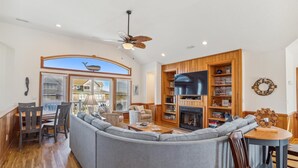 A spacious living room with a large gray sectional sofa, wooden flooring, a ceiling fan, and a fireplace. - 220ft from beach access! Private pool, hot tub. Summer deals! (Corolla)