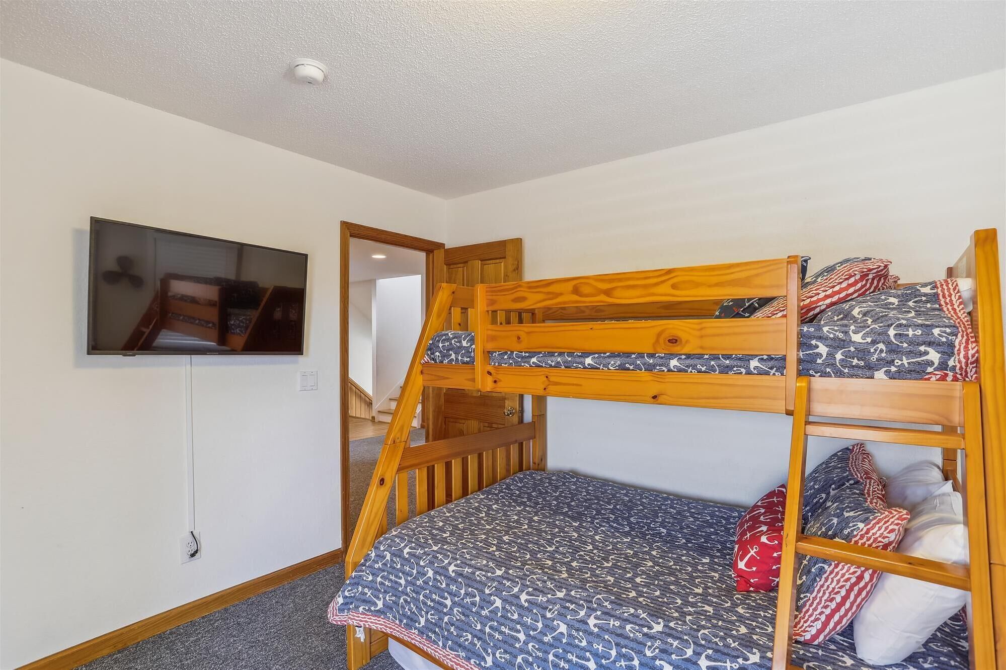 A bunk bed with a patterned bedspread, a television mounted on the wall, and a ceiling light.
