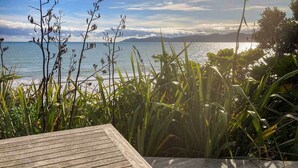 A wooden deck overlooking a coastal view with vegetation in the foreground. - Seascapes Waterfront 2 (Paraparaumu)