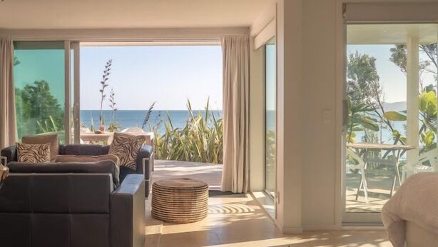 A modern living room with a large sliding glass door leading to a balcony with a view of the sea. - Seascapes Waterfront 2 (Paraparaumu)