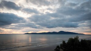 A coastal landscape with a calm sea, distant mountains, and a cloudy sky. - Seascapes Waterfront 2 (Paraparaumu)