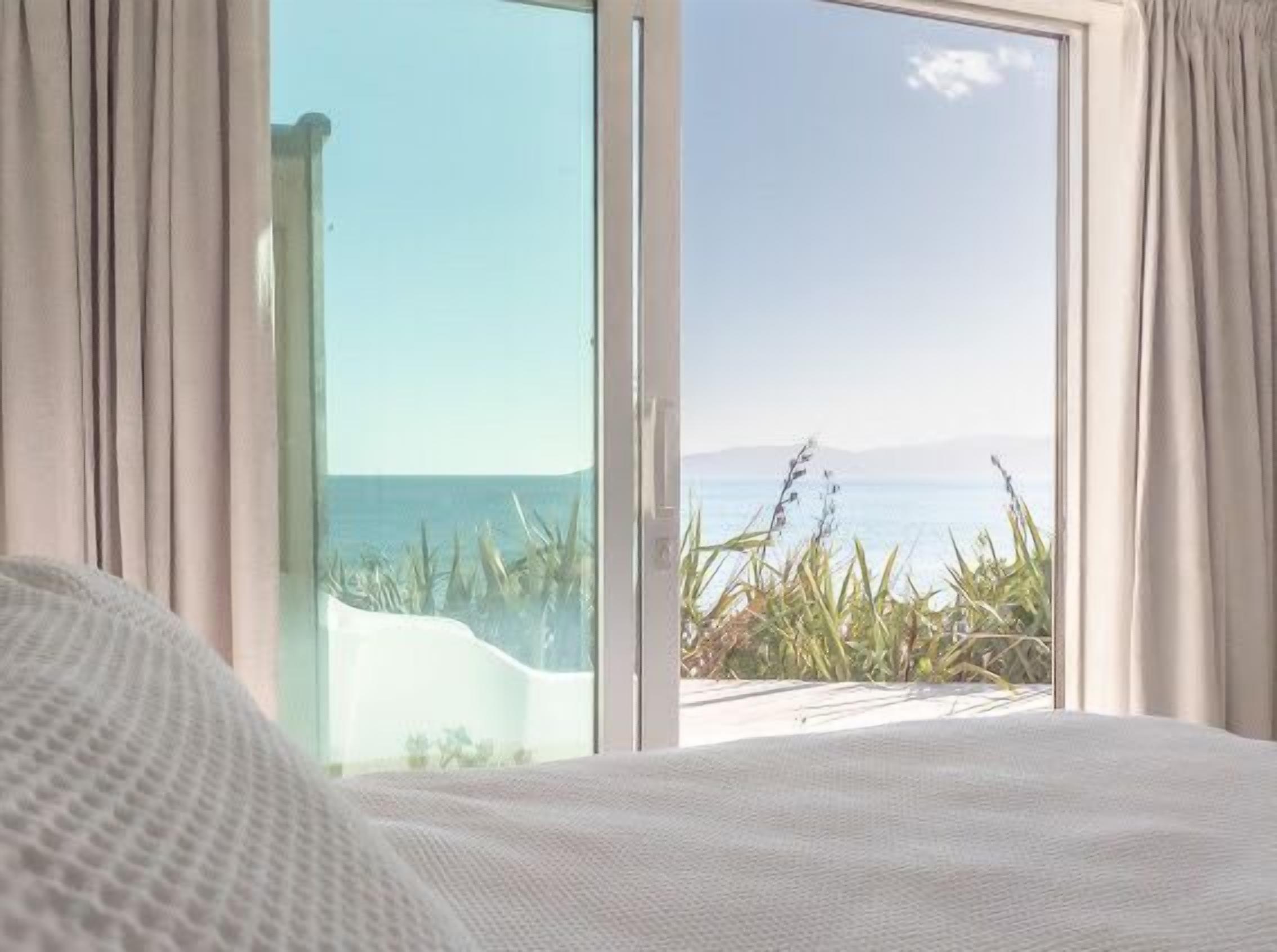 Un dormitorio con una cama grande, vista al mar a través de un ventanal corredero y cortinas a ambos lados.
