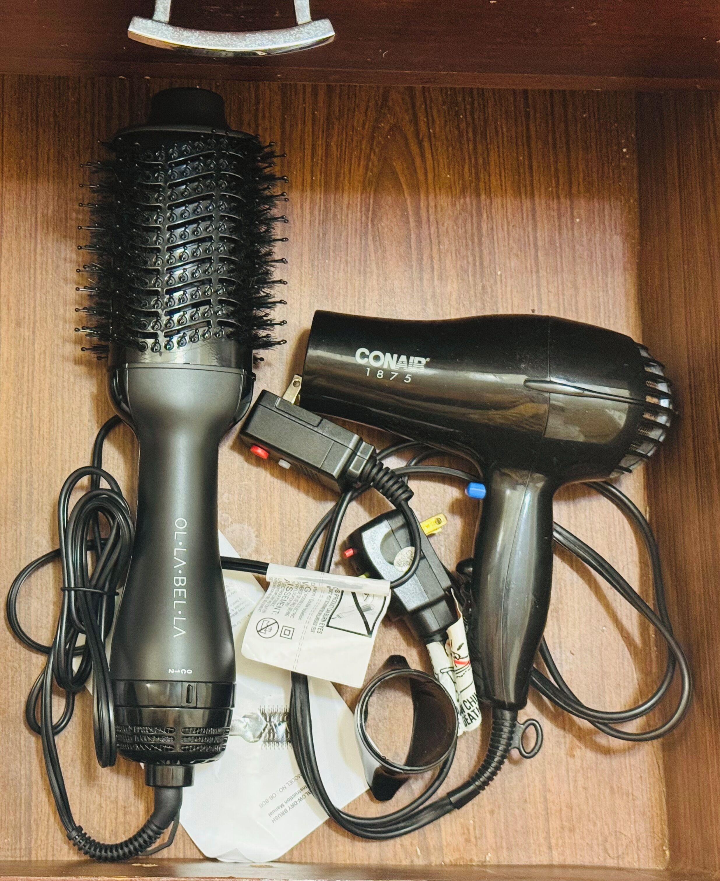 A drawer containing a hairdryer, a brush, and a power strip with cables.