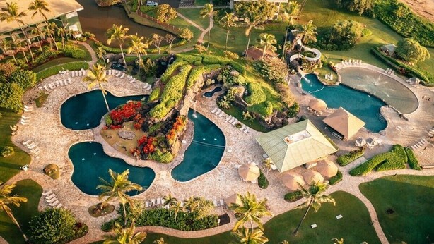 Vista aérea de um resort com várias piscinas, palmeiras e jardins bem cuidados.