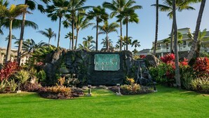 Placa do Kauai Beach Resort cercada por vegetação tropical e palmeiras.