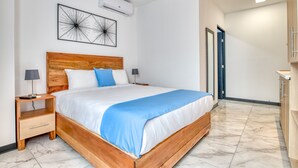 A modern bedroom with a wooden bed, a nightstand, a wall-mounted air conditioner, and a door leading to another room. - Private Apartment in the Heart of San Jose! (San Jose)