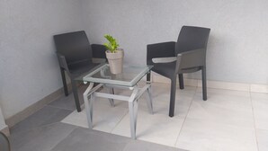 Un pequeño espacio exterior moderno con dos sillas y una mesa de vidrio, con una planta en maceta.