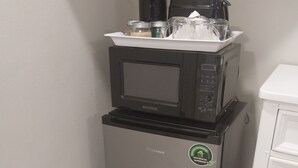 Un refrigerador compacto con un microondas encima, una cafetera pequeña y un dispensador de agua.