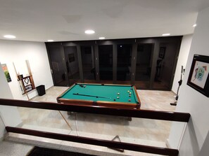 Una mesa de billar en una habitación con un separador de vidrio y un cuadro en la pared.