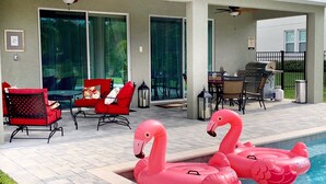 Ein Poolbereich mit zwei Flamingo-Schwimmpfauen, roten Stühlen, einem Tisch mit Stühlen und einem Grill.