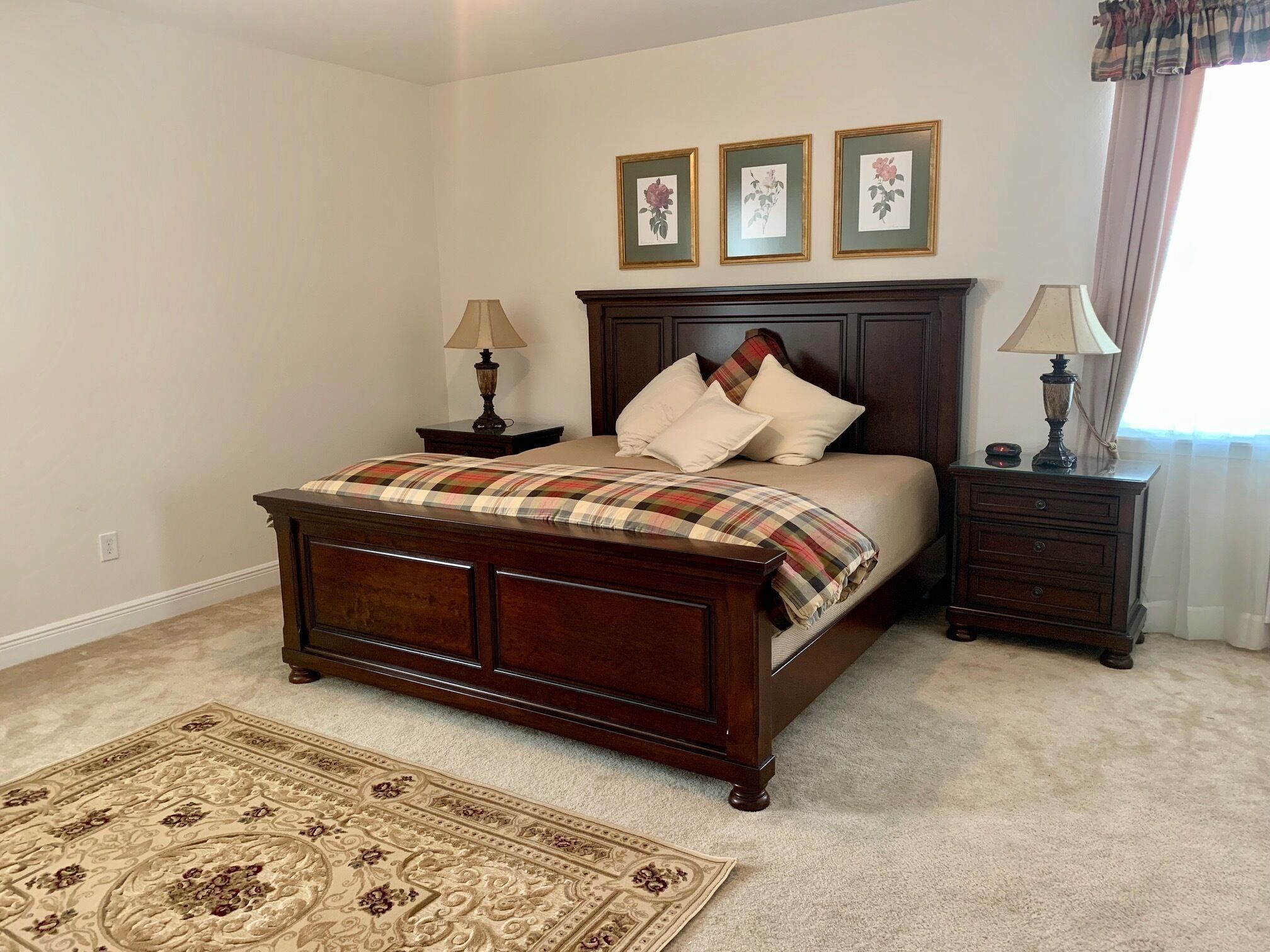 Un dormitorio con una cama grande, dos mesitas de noche, un cabecero de madera, un tapete decorativo y tres cuadros enmarcados en la pared.
