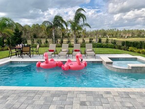 A swimming pool with two pink flamingo floats, lounge chairs, and a table with chairs.