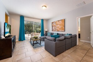 Relax in this stylish living room with a large sofa, flat-screen TV, and abstract art, leading to a patio with outdoor furniture.