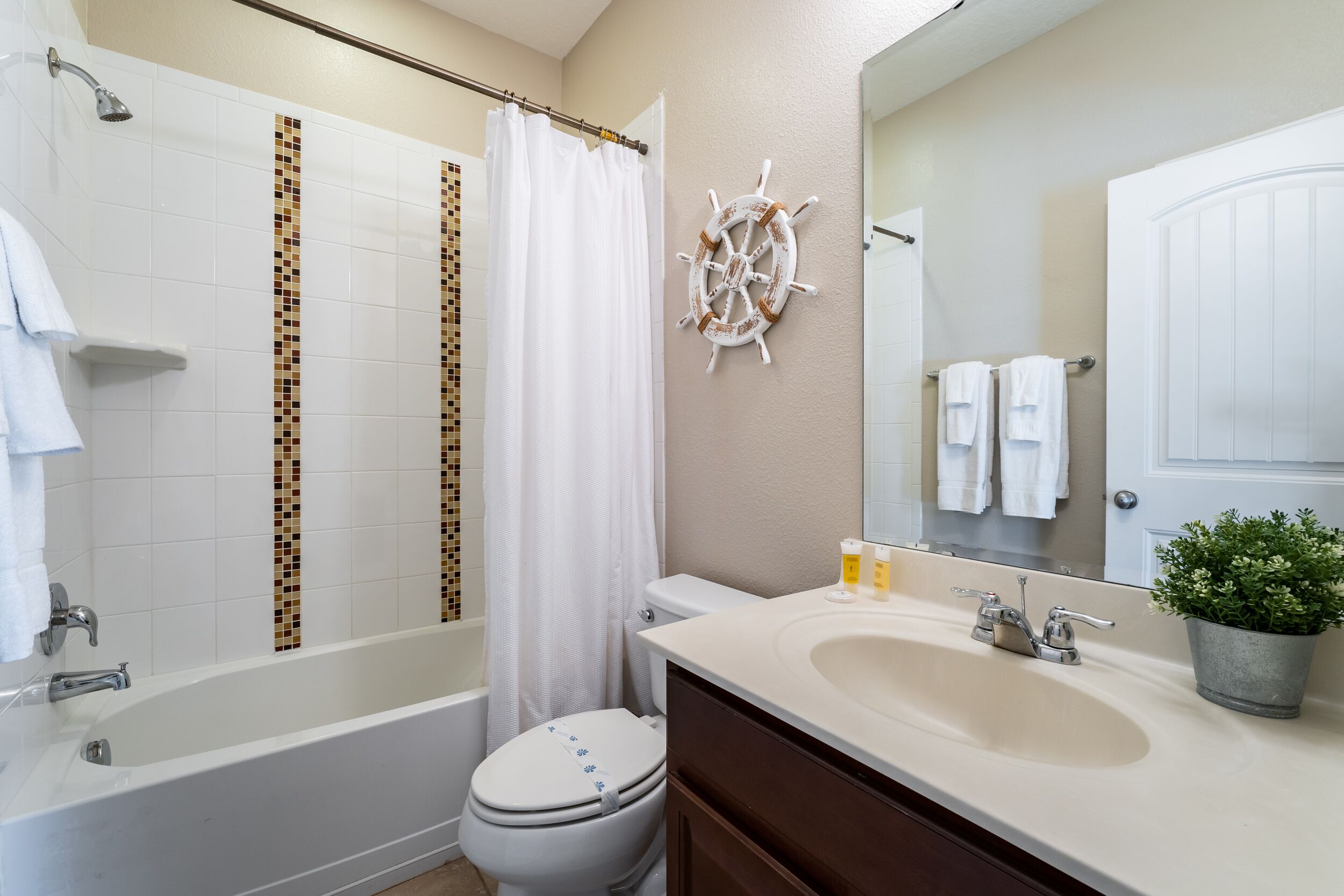 A bathroom with a bathtub, toilet, sink, and a ship's wheel decoration.