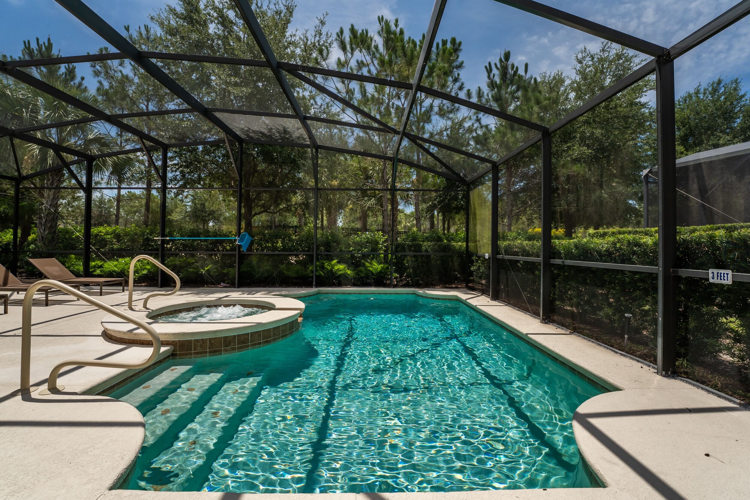 Piscina descoberta coberta com hidromassagem, cercada por grade de metal e vegetação exuberante.