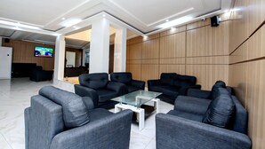 A modern lobby with grey sofas, a glass coffee table, and a TV mounted on the wall. - Hotel Galilée (Cotonou)