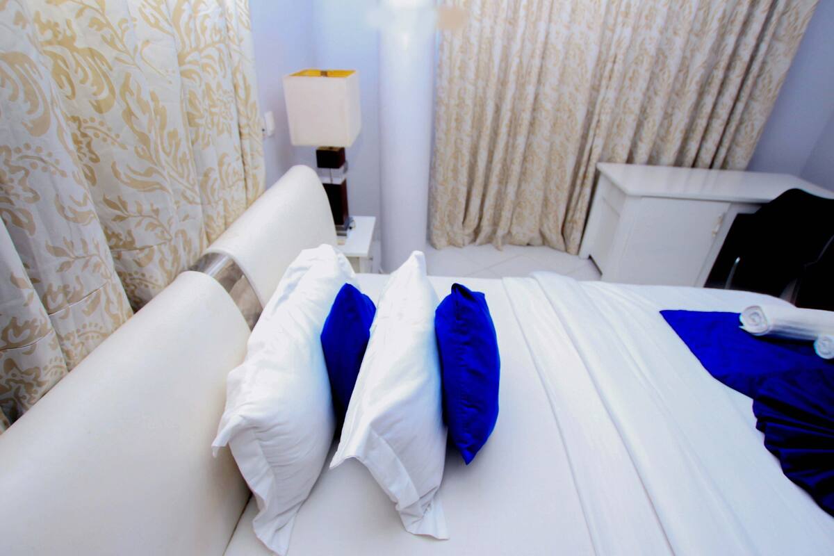 Una habitación de hotel con una cama, cortinas blancas, una lámpara y un ventanal con cortinas.