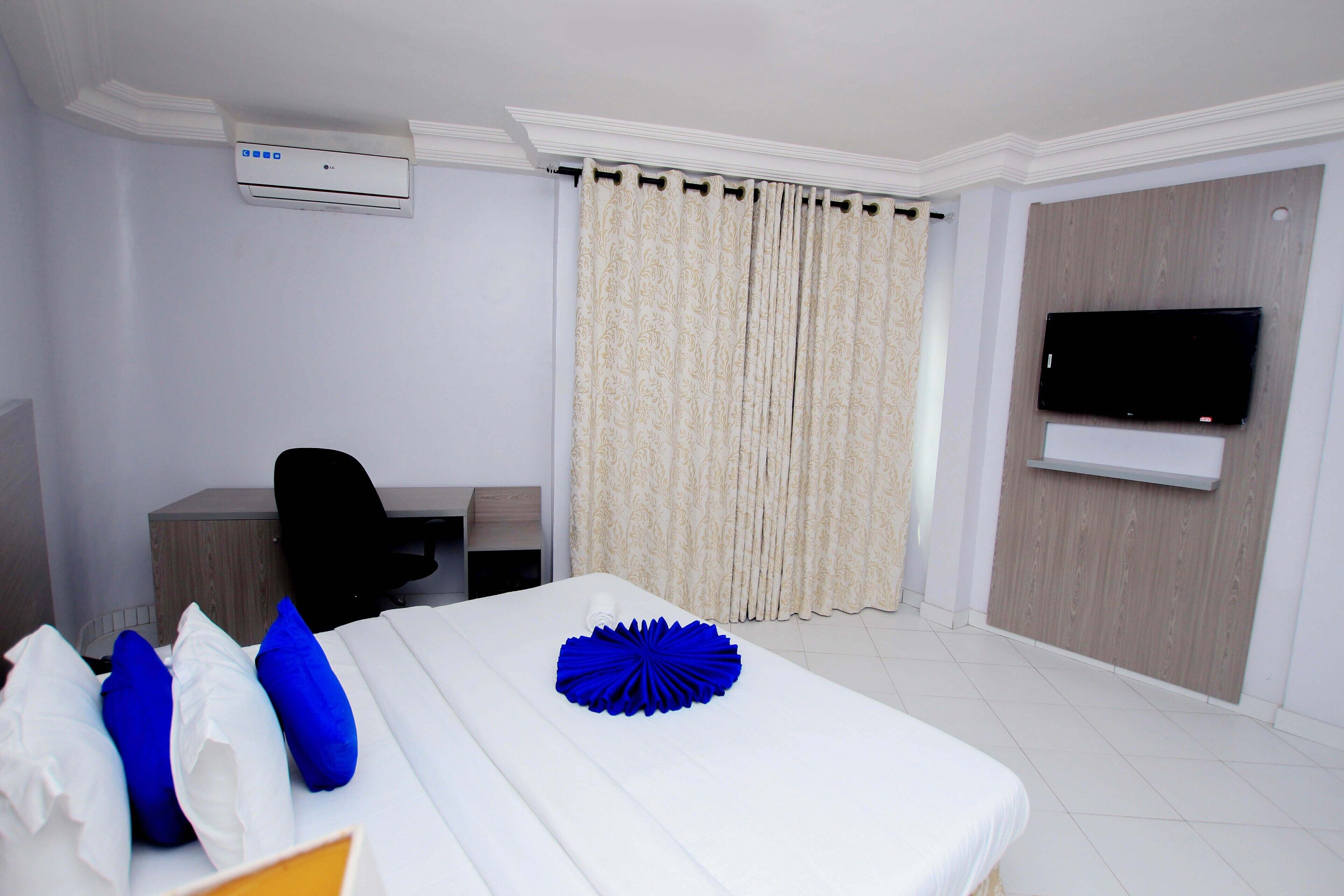 Habitación de hotel con cama, escritorio, silla, televisión de pantalla plana y ventana con cortinas.