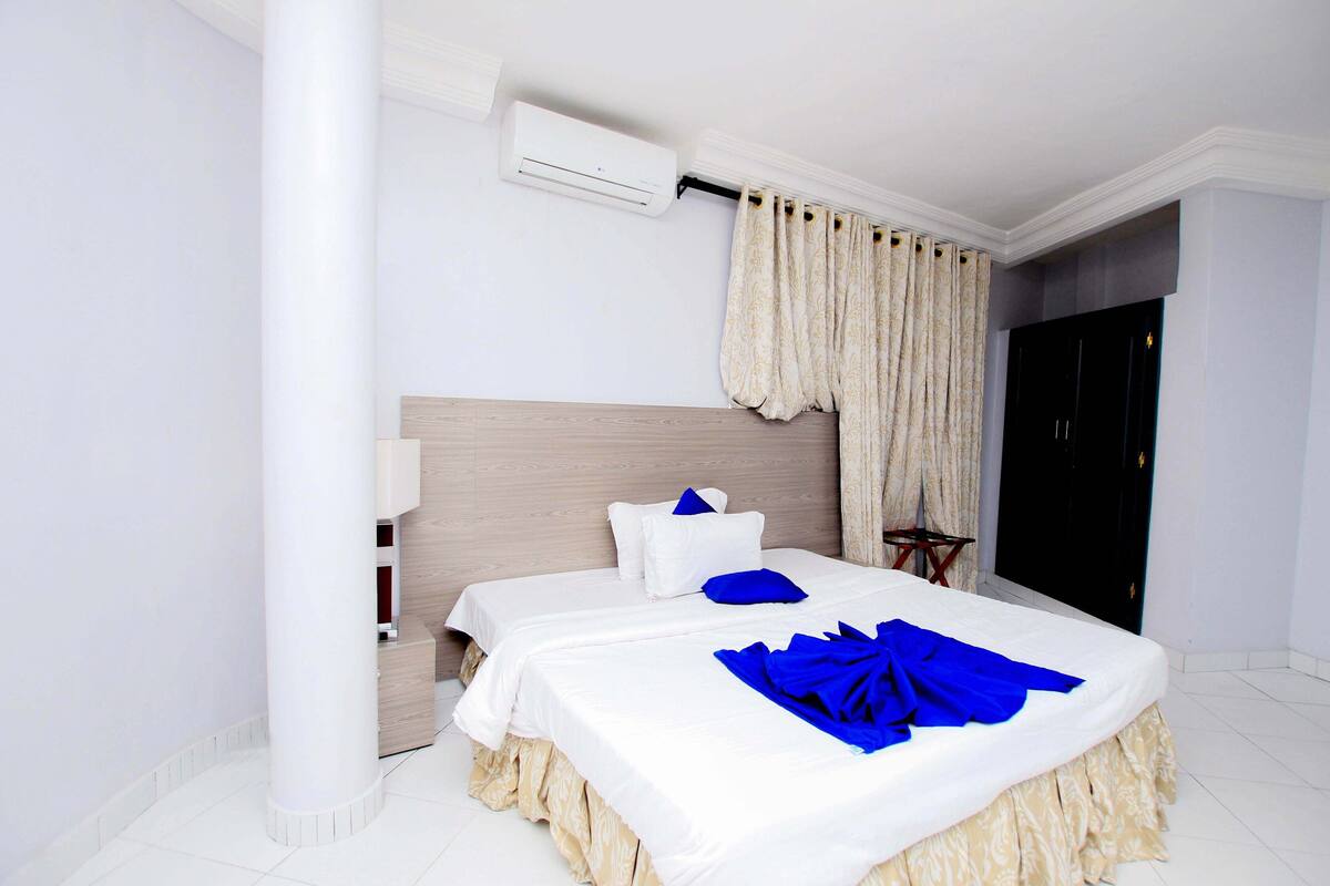 Una habitación de hotel con dos camas, un ventanal con cortinas, un aire acondicionado y un armario.