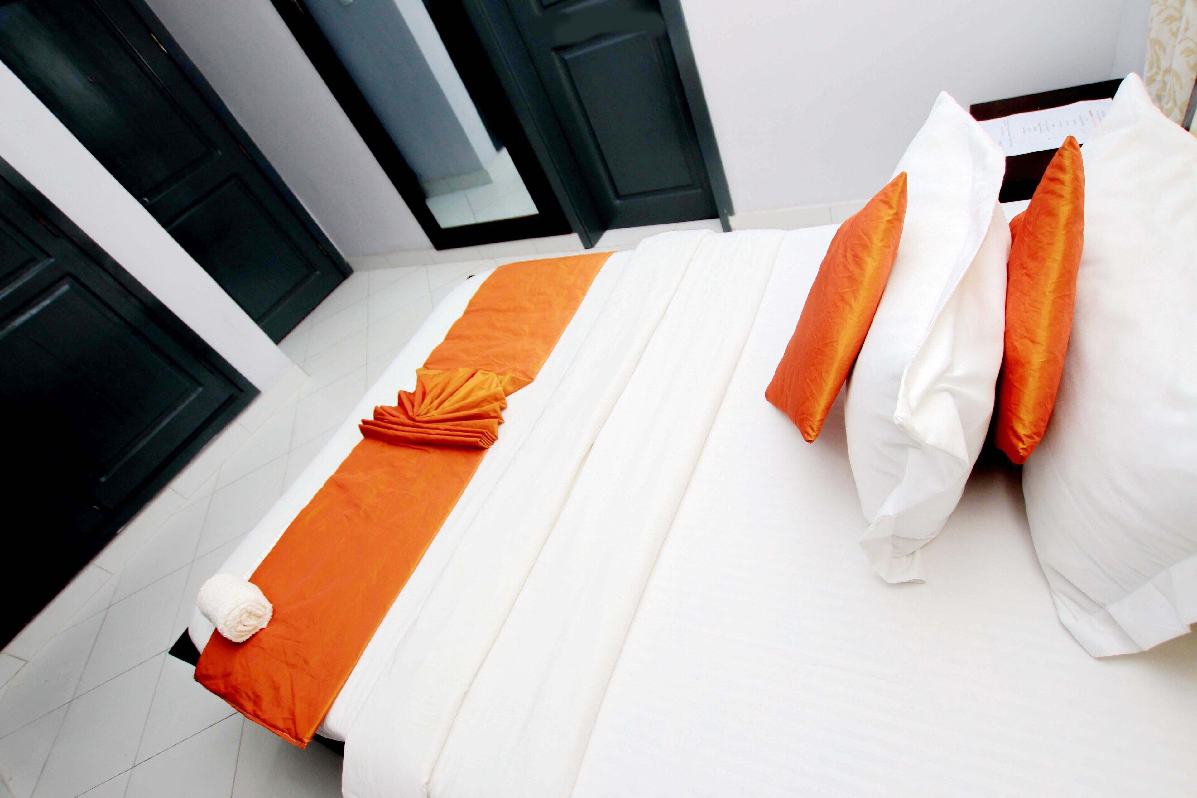 Uma cama bem arrumada com roupa de cama branca e laranja, um travesseiro branco e uma toalha laranja dobrada.