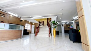 A hotel lobby with a reception desk, a staircase, and a seating area. - Hotel Galilée (Cotonou)