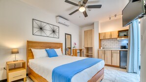 Un dormitorio con cama, mesitas de noche, ventilador de techo y una kitchenette con armarios y microondas.
