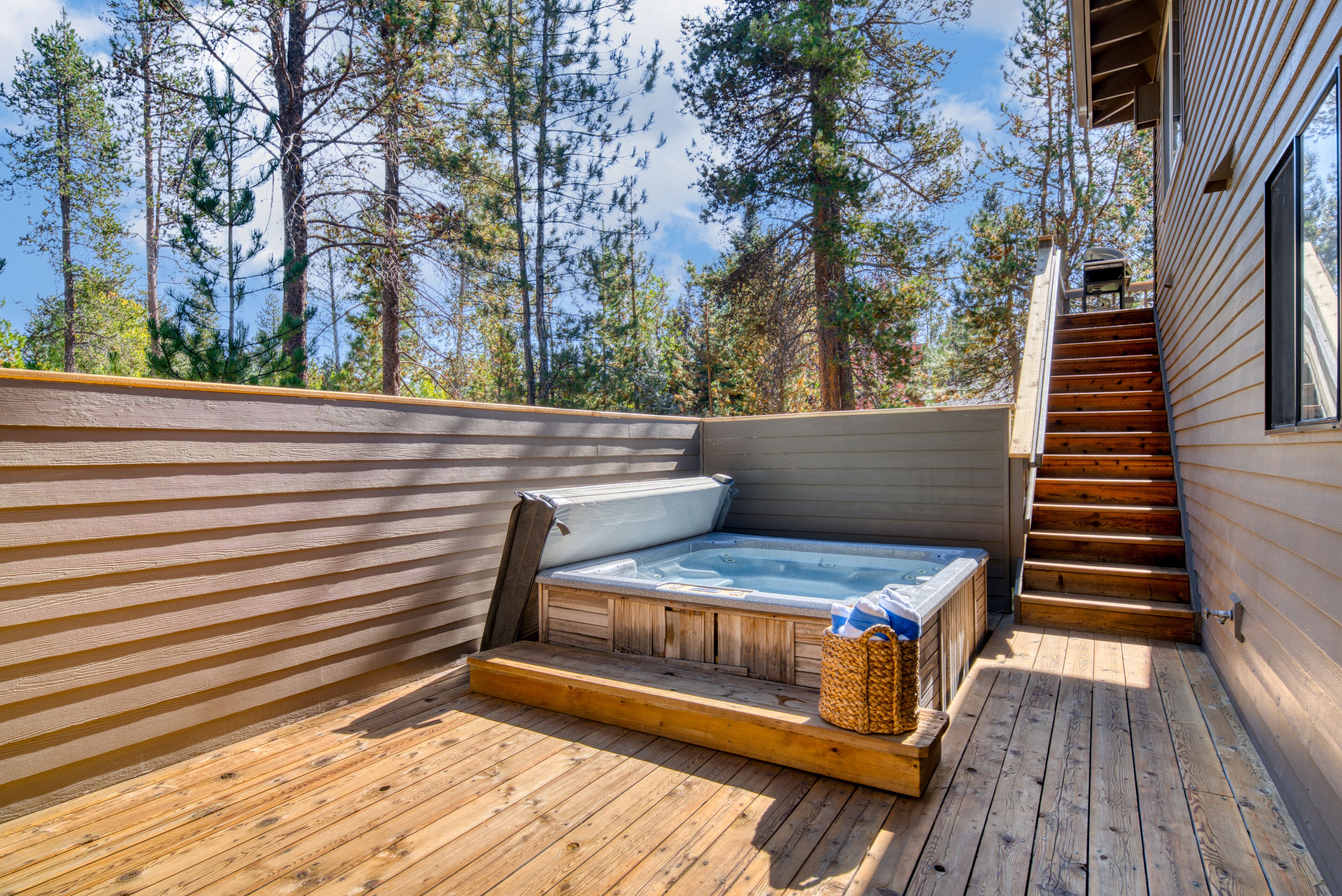 Eine Holzterrasse mit Whirlpool, Holztreppe und Blick auf hohe Kiefern.
