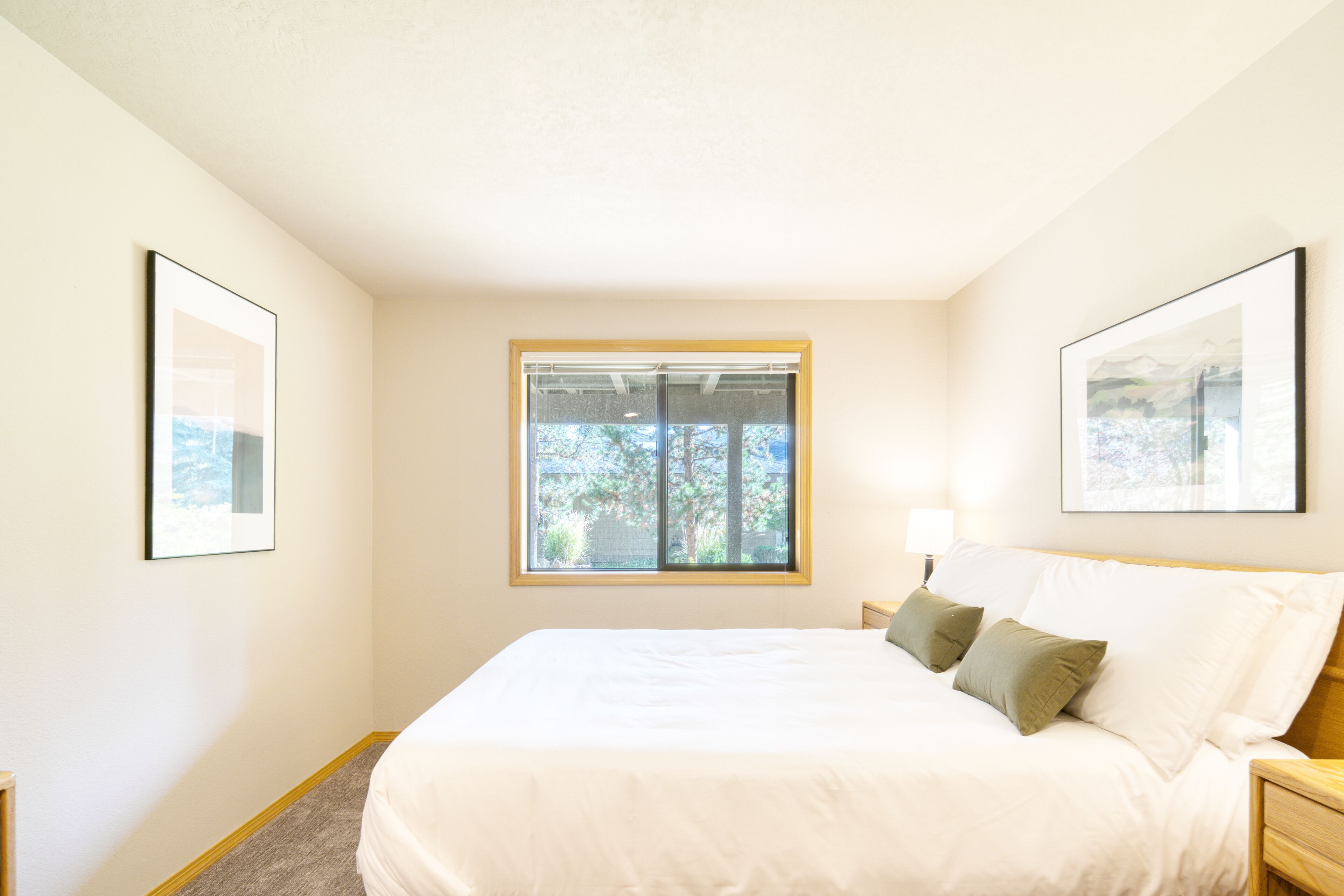 A bedroom with a large bed, a window, and two framed pictures on the walls.
