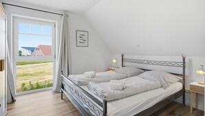 A bedroom with a bed, a nightstand, a lamp, a window with curtains, and a view of the outside.