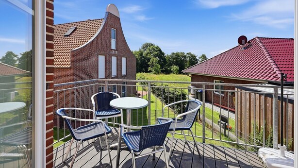 A balcony with a table and chairs, a view of a brick building, and a red-roofed structure.