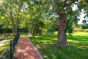 Ein gepflasterter Weg führt durch einen Park mit Bäumen und einer Rasenfläche.